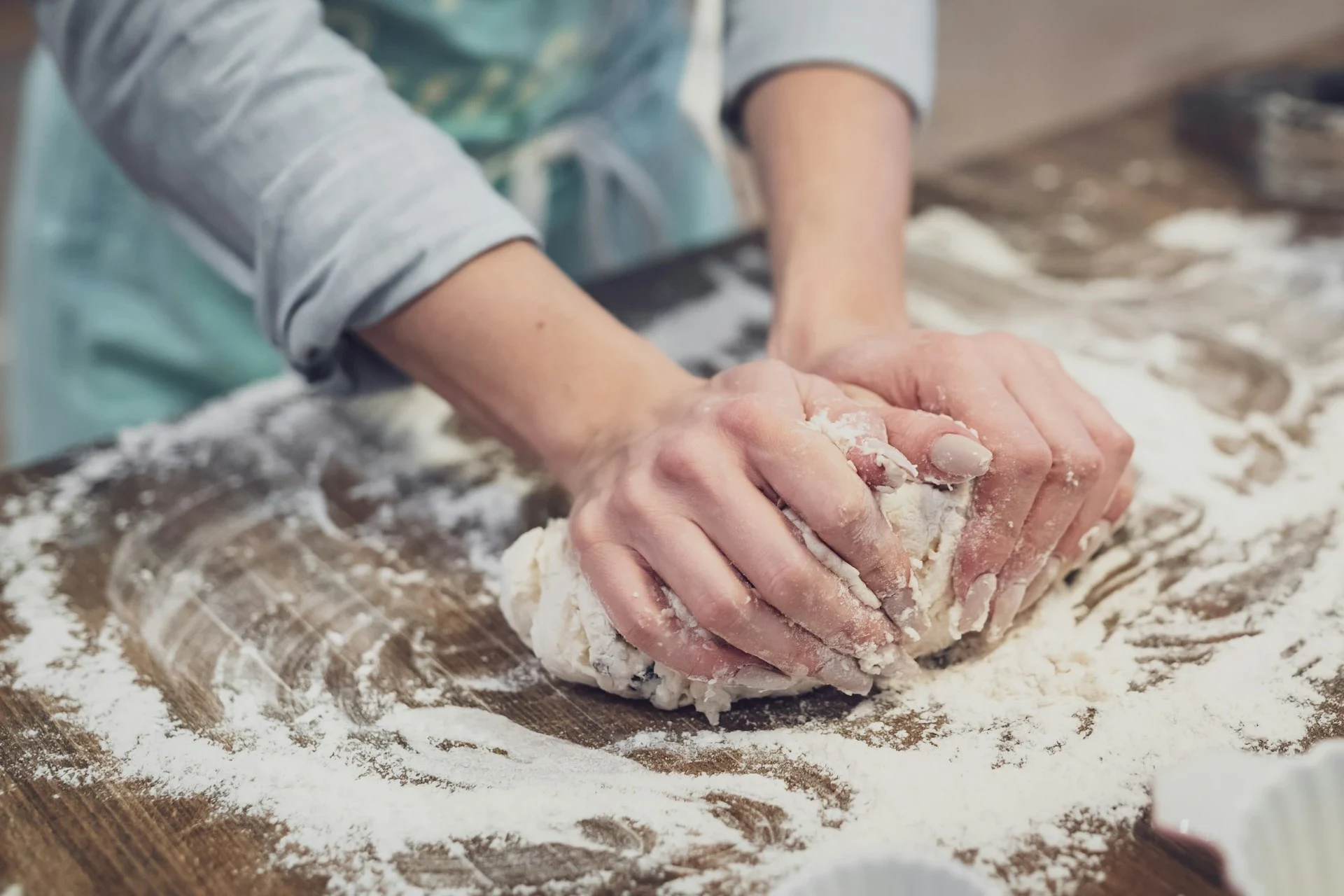 A baker kneading dough on a floured wooden counter.