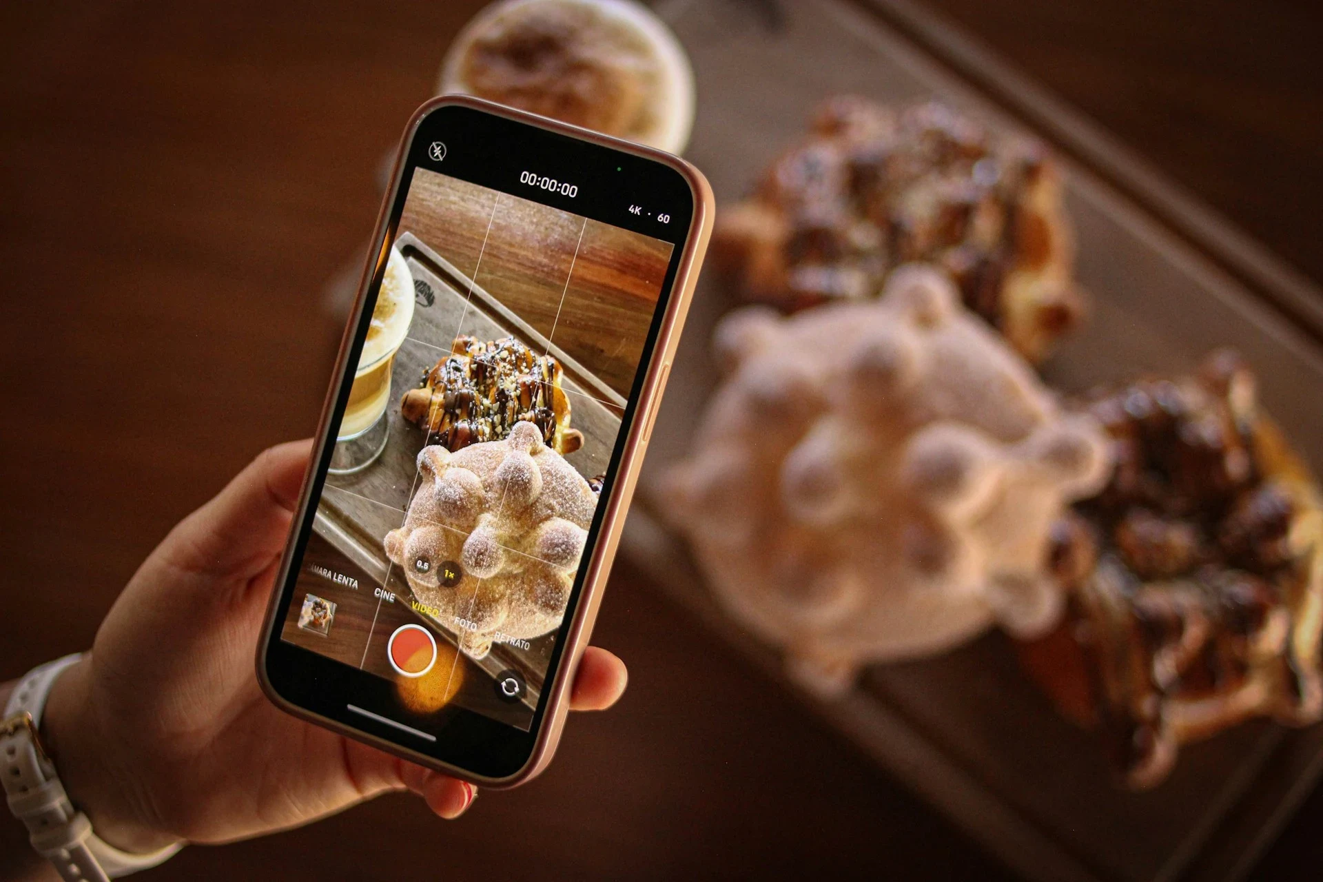 A hand holding a phone, photographing a table of fresh pastries.